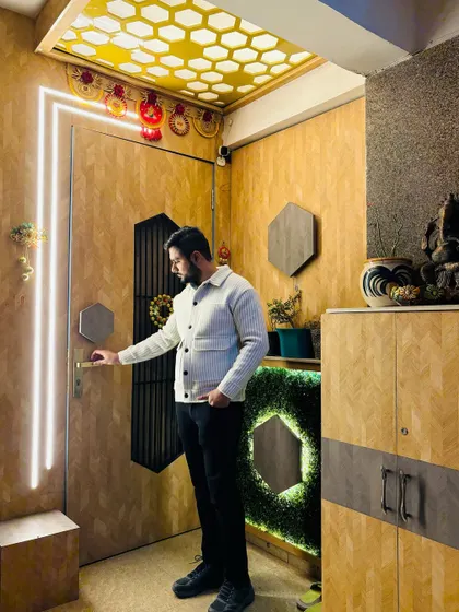 A stunning entrance at a Prateek Laurel project. The design features a wooden door with vertical light strips, a hexagonal-themed ceiling, and a matching shoe cabinet with a green moss accent.