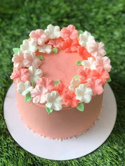 A simple and sweet peach-colored cake with a wreath of hand-piped white and pink flowers.