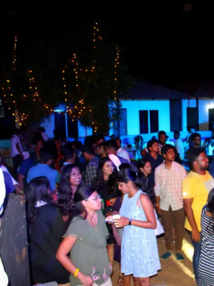 A wide shot of a beach party at night, with fairy lights and a crowd of people enjoying the music and atmosphere.