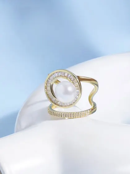 This creative shot places a pearl and diamond ring on a white abstract prop. The composition against the light blue background is modern, clean, and artistic.