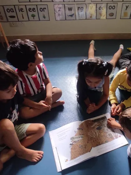Children look up at the phonics chart on the wall while listening to a story, making connections between the sounds they hear and the letters they see.