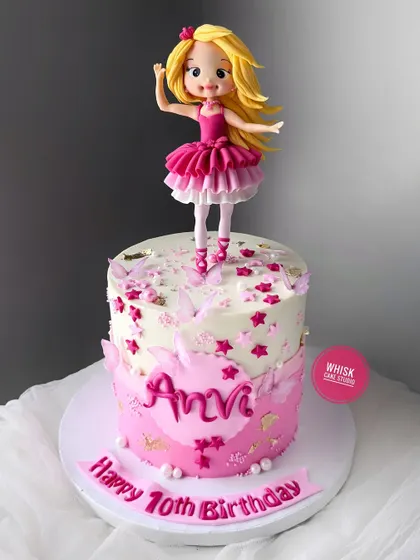 A pretty pink Barbie cake for a 10th birthday. This design features a handcrafted ballerina Barbie doll on top of a cake decorated with pink stars and butterflies.