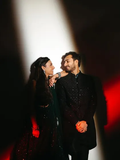 A dramatic and stylish sangeet portrait using creative lighting. The red and white light casts an artistic glow, highlighting their modern and chic wedding style.