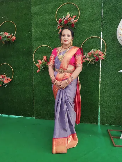 A full-length view of a client ready for a family event. Her makeup is elegant and polished, perfectly matching her grey and pink silk saree and traditional jewellery.