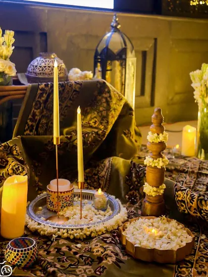 A beautiful tablescape with traditional elements. A silver tray holds taper candles and jasmine, surrounded by patterned fabrics and wooden decor for a warm, inviting feel.