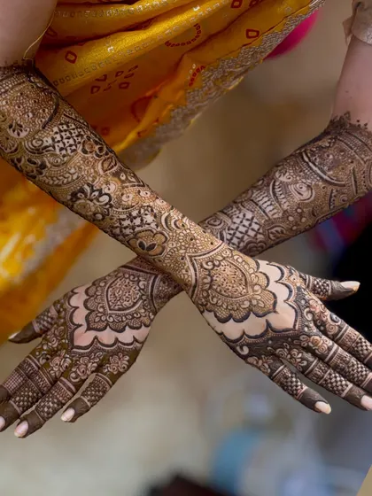 A beautiful crossed arm pose from bride Hajira, showing off her full bridal henna. The design features large mandala-like patterns on the back of the hands, complemented by detailed work up the arms.