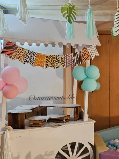 A themed cart is ready to serve treats, decorated with an animal-print banner and pastel balloons, fitting seamlessly into the jungle decor.