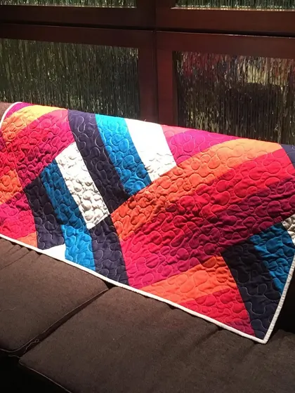 The modern striped quilt draped over a sofa, showing how it can add a pop of color to any room.