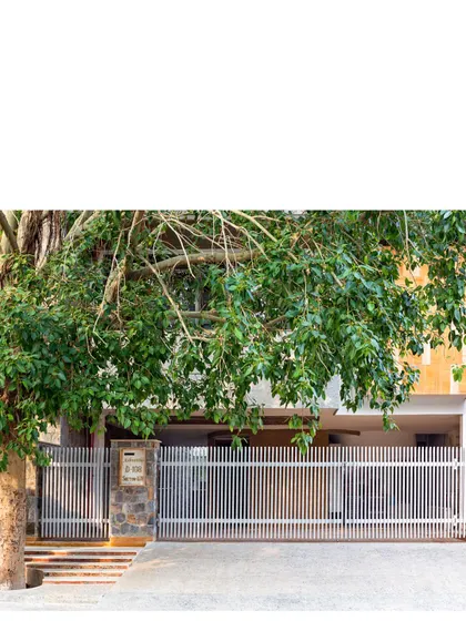 The entrance to 'Ashvattha', the People Tree House, is framed by the sacred fig tree itself. The design of the gate and entryway is intentionally subtle, allowing the natural beauty of the tree to remain the main focus and signaling the home's core philosophy of harmonious living from the very first impression.