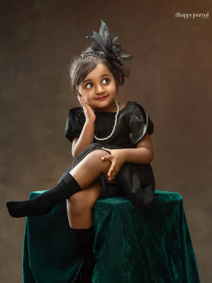 A little fashionista in a black dress and fascinator hat, striking a thoughtful pose. This portrait is full of personality and vintage charm.