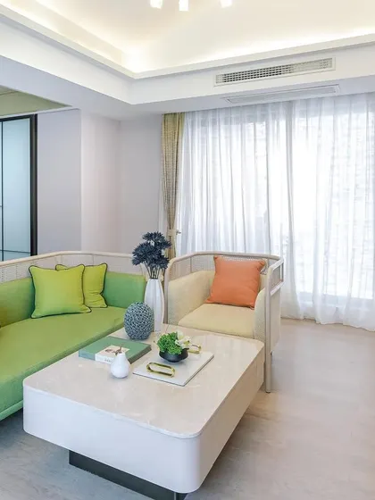 Another view of the minimalist living space, showcasing a green L-shaped sofa with pops of bright color from the cushions. The design emphasizes clean lines and an uncluttered feel.