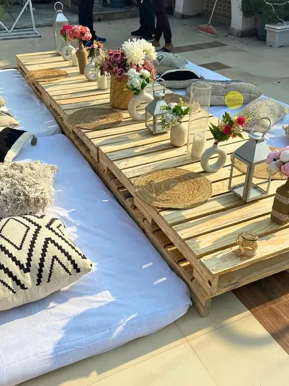 A detailed look at our boho sit-down tablescape. We use wooden pallets for the table, surrounded by an assortment of comfortable and stylish cushions and decorated with simple floral arrangements and lanterns.