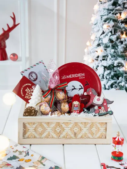 The 'Winter Wonderland' hamper fully assembled in a woven wooden box, set against a snowy Christmas tree backdrop for a magical, festive feel.
