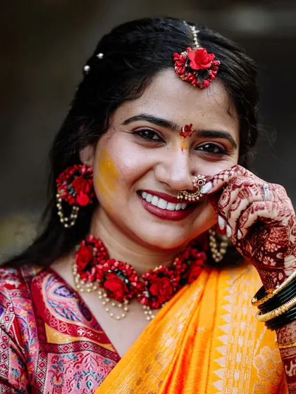 A close-up portrait of the bride, smiling and playfully touching her floral nose ring.