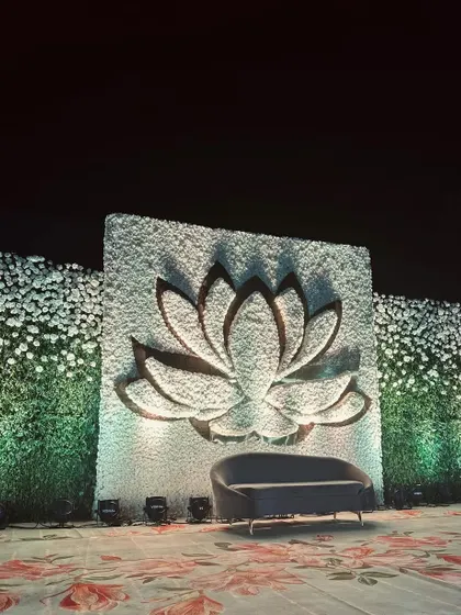 A minimalist yet striking stage design featuring a large 3D lotus cutout against a wall of white flowers. The clean lines and focused lighting create a serene and elegant photo backdrop.
