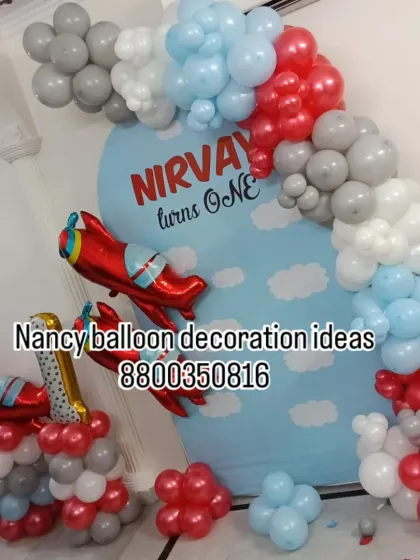 An adventurous airplane theme for a first birthday party. This setup includes a sky-themed backdrop, red airplane foil balloons, and a balloon arch in red, grey, and light blue.