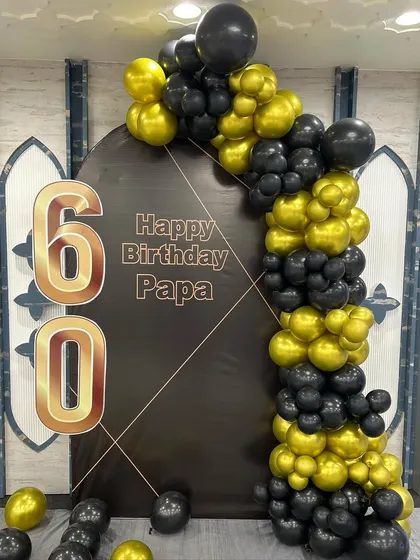 A classic and stylish 60th birthday decoration for a father. This simple setup features a black arched backdrop with 'Happy Birthday Papa' and a sophisticated black and gold balloon garland.