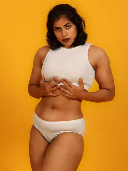 A bold and unapologetic portrait celebrating the female form. The simple white garments against a vibrant yellow background create a high-impact, minimalist statement.