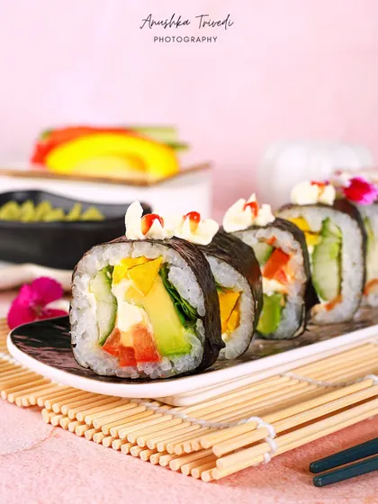 Fresh vegetable sushi rolls on a bamboo mat, shot against a soft pink background for a bright and clean look.