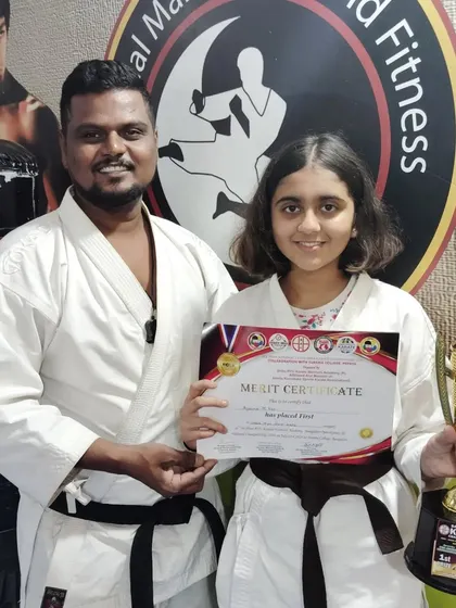 This brown belt student smiles with her first-place certificate and trophy, a significant achievement in her karate journey.