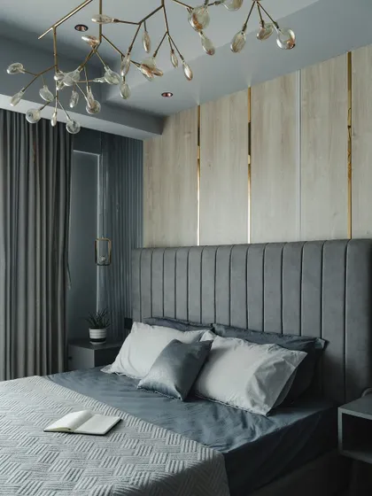 A sophisticated bedroom featuring a vertically channeled grey headboard set against a wall with wood and metallic-accented panels. The unique branch-like chandelier adds an artistic, organic touch.