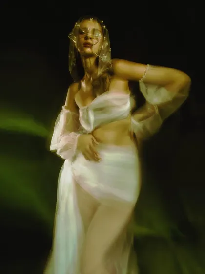 A painterly portrait with soft motion blur, capturing the model in a flowing white garment. The greenish light and soft focus give the image a dreamlike, ethereal quality.