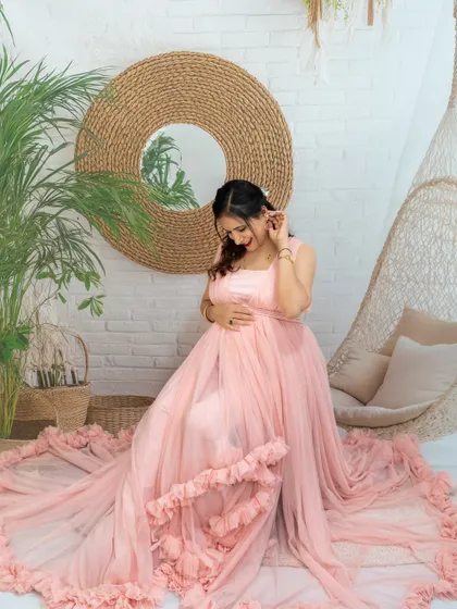 A serene portrait of a mom-to-be in a pink gown, looking down at her bump in our boho studio setup.