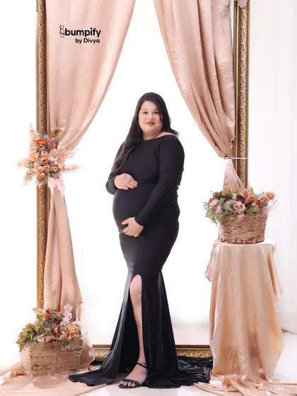 A confident solo portrait of the mom-to-be in a classic black gown. The soft pink drapes and floral arrangements add a touch of romance to the scene.