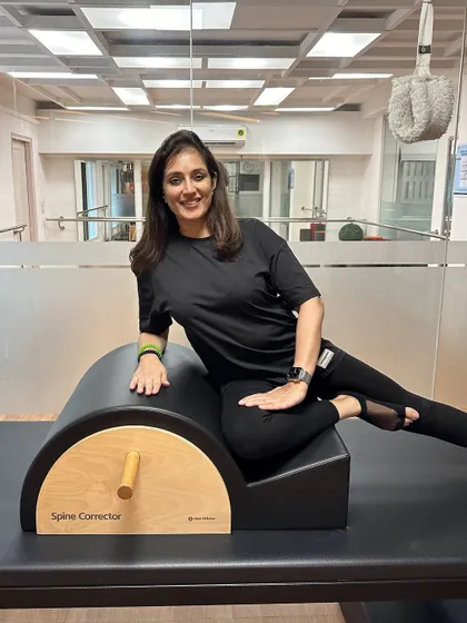An instructor smiles while resting on the Spine Corrector, a piece of equipment used to improve posture and spinal health.