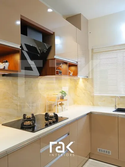 A closer look at the cooking area in the Kakkanad villa kitchen, with a modern hob and chimney set against a warm, veined backsplash.