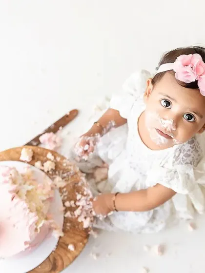 A high-angle shot capturing the aftermath of a fun cake smash, with the baby looking up from her messy masterpiece.