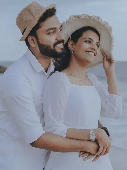 A sweet and happy couple enjoying a moment on the beach, dressed in white and wearing straw hats.