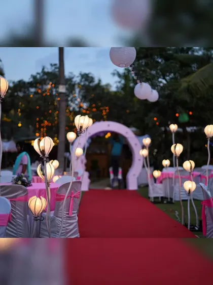 A red carpet aisle for a birthday party, lined with whimsical flower-shaped lamps and white paper lanterns hanging above. This decor creates a fun and celebratory pathway for the guests.