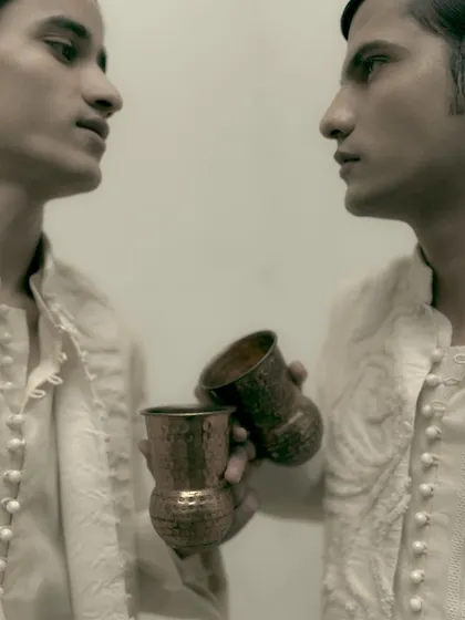 A sepia-toned dual portrait for Sanchit Sharma. The close, mirrored composition creates an intimate and slightly surreal feel, focusing on the models' profiles and the garment details.