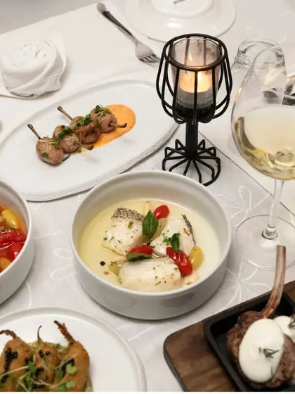 A table set for a candlelight dinner, featuring a variety of our small plates and main courses, including lamb chops and a delicate fish dish.