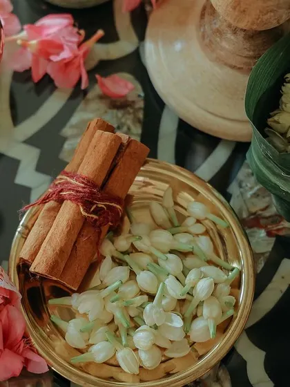 A beautiful flat lay of traditional items, including cinnamon sticks, jasmine buds, and pink flowers in brass bowls. The colors and textures are vibrant and inviting.