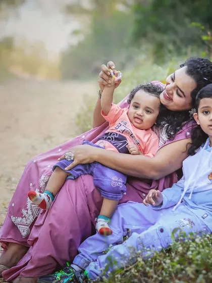 A mother sits on a dirt path with her two sons, one a toddler and the other a young boy. The composition feels natural and relaxed, telling a story of a mother's love for her children.