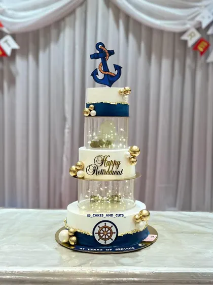 A full view of the illuminated navy retirement cake, showing the anchor and ship's wheel details. The fairy lights add a magical touch to the celebration.