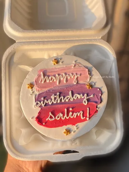 A colorful painted bento cake with a personalized birthday message. The blend of pink, purple, and red creates a beautiful sunset effect.