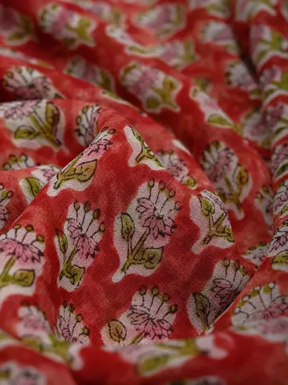 A close-up of a red block-printed georgette fabric. The lightweight material and vibrant print make it ideal for creating beautiful, flowing party sarees.