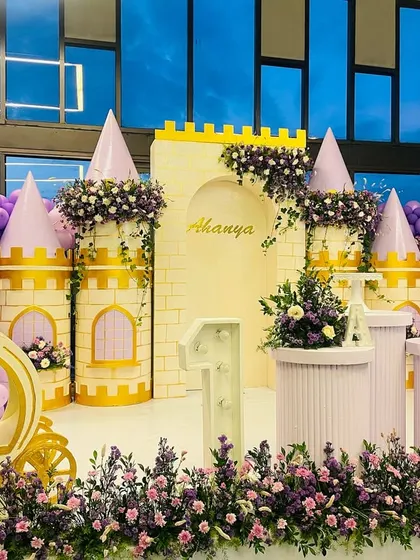 The complete setup for a magical princess party, featuring a custom castle, a royal carriage for photos, and beautiful floral arrangements in shades of purple.