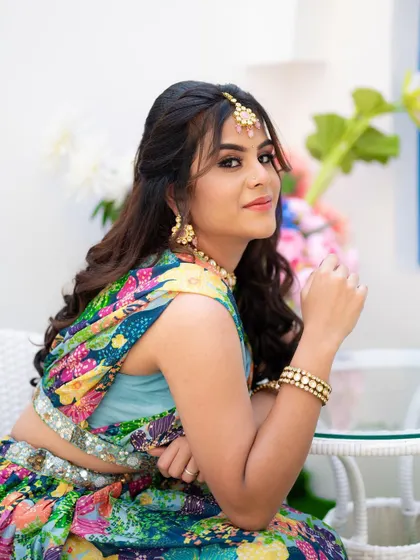 A relaxed, seated portrait during the Mehendi festivities. The composition is clean and elegant, focusing on her colorful outfit and happy expression.