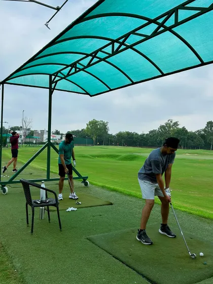 Three golfers practicing side by side under a covered bay, showcasing a typical group setup.