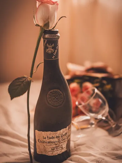 A romantic, vintage-inspired shot of a wine bottle and a single rose for Valentine's Day. The moody lighting and soft textures create a timeless and intimate feel, perfect for luxury or gifting brands.