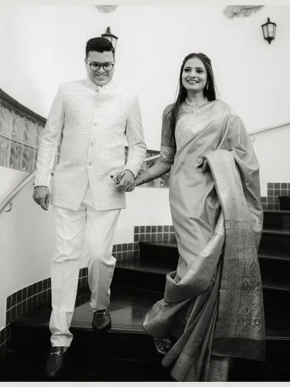 A classic black and white photograph of a couple descending a staircase, holding hands. The elegant composition and their formal attire give this shot a timeless, graceful feel.