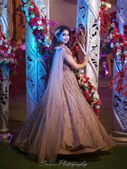 A full-length portrait of the bride posing by ornate pillars and floral decorations at her engagement venue.