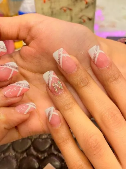 A modern French manicure with a twist. This set features a crisscross white line design over the tips, with one accent nail adorned with a small cluster of crystals.