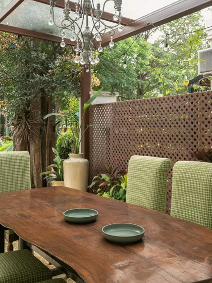 Adjacent to the bar, a live-edge dining table with a raw, organic grain is surrounded by green houndstooth chairs. An antique crystal chandelier adds a touch of whimsical contrast to the rustic setting.