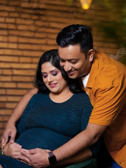 A sweet, intimate moment captured during a studio session. The couple looks down at the baby bump together, sharing a private moment of connection.