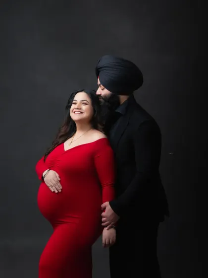 A joyful and elegant couple's portrait. The mother-to-be's bright smile and the classic red and black attire make for a timeless and happy memory.